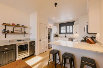 Modern kitchen with white countertops, breakfast island, barstools, and wet bar at Campfire Cabin at See Forever.