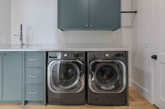 A modern laundry room at SkyRidge 1152 featuring a dark graphite LG washer and dryer, custom sage green cabinets, and a white marble countertop.