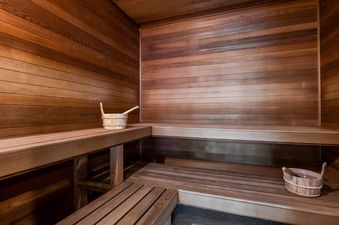 A private sauna room with wooden paneling, multi-level benches, and a wooden bucket with a ladle for a traditional sauna experience.