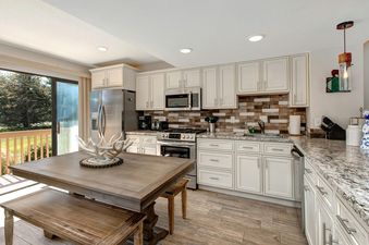 A kitchen with white cabinets, stainless steel appliances, and granite countertops. There is a dining table and bench in the foreground.