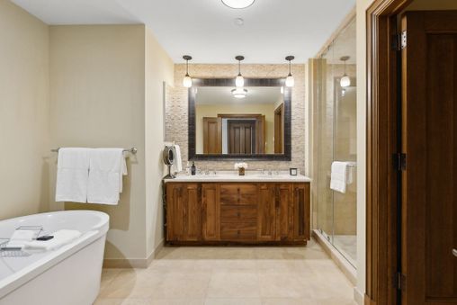 A bathroom with a white soaking bathtub, a large mirror, and a double vanity with wooden cabinets.