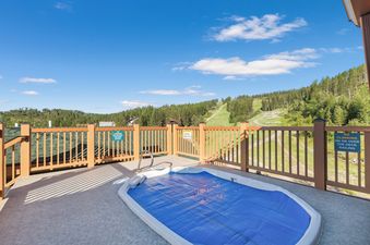 A private hot tub on a deck overlooking a mountainous landscape with ski slopes, set under a clear blue sky, at Morning Eagle 209.