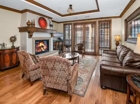 The inviting living area of Arrabelle 460 features a cozy fireplace, comfortable armchairs and sofa, and elegant wooden furnishings under natural light from large windows.