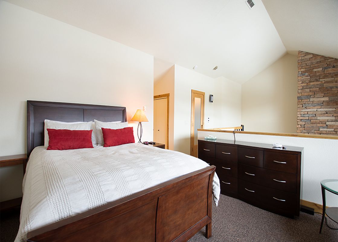 The bedroom features a comfortable bed with red pillows and a wooden frame, along with a dresser and a small table.