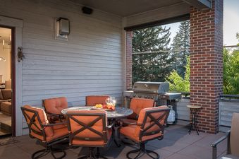 Covered outdoor patio of 5th Street Penthouse with an outdoor dining table, chairs, and a BBQ grill.