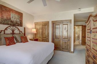 A luxurious bedroom at Arrowhead Village Condominium Premium 3 Bedroom, featuring a king-sized bed with an ornate metal headboard, two wooden closets, and a view into an en-suite bathroom.