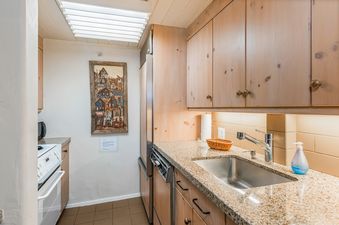 The kitchen at Row House 3 Bedroom Gold Unit 6B features wood cabinetry, a granite countertop, and a stainless steel sink with a modern faucet.