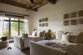 A bright guest bedroom at Le Refuge featuring two queen beds, a wooden ceiling, and a large window with scenic views.