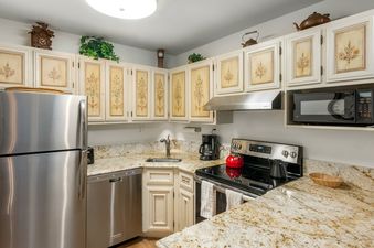The kitchen at Chateau Christian 2 Bedroom Gold Unit 220 features white cabinets with floral designs, granite countertops, and stainless steel appliances.