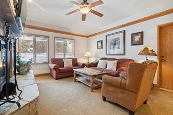 A cozy living room at The Charter F2105 with a fireplace, comfortable seating, and windows looking out onto a snowy exterior.