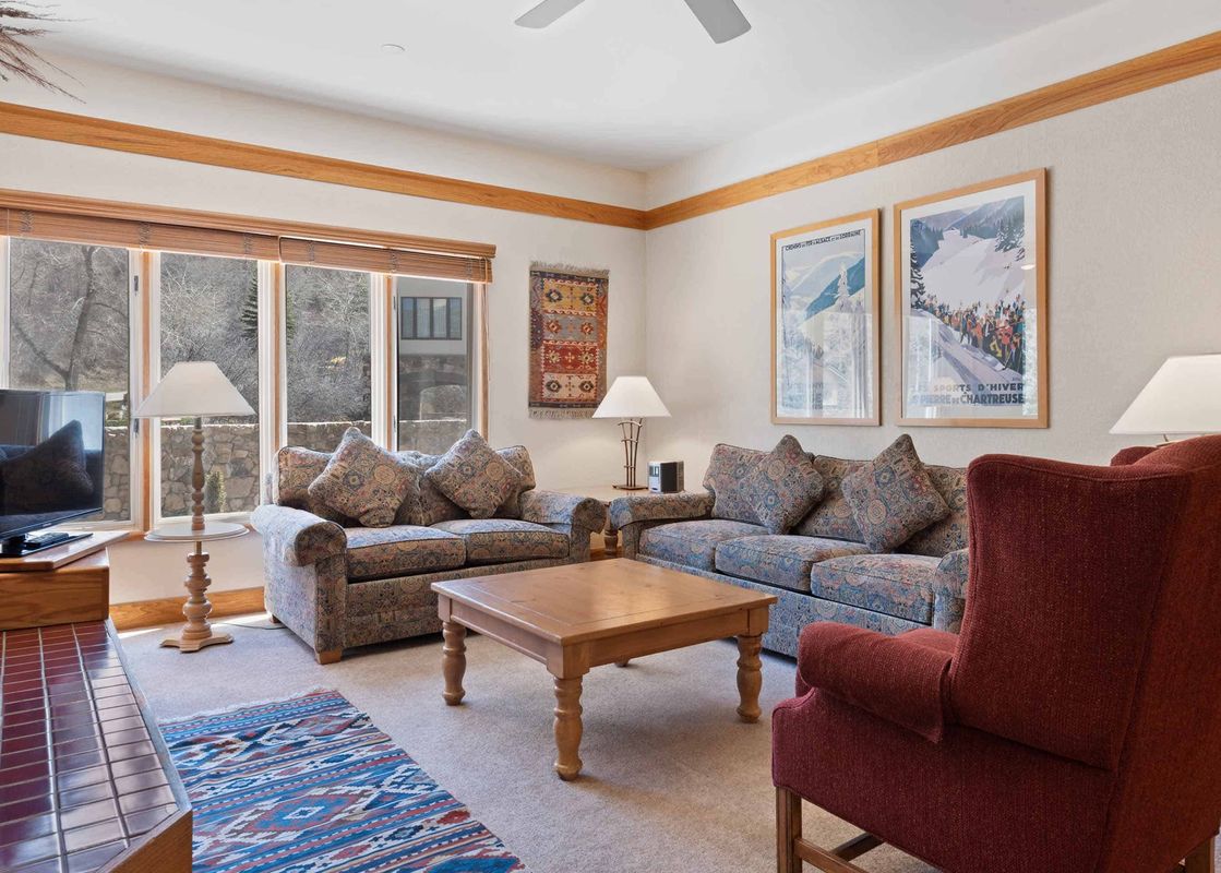 A cozy lounge area in The Charter F3305 with two patterned sofas, a wooden coffee table, a red armchair, and multiple windows providing natural light and an exterior view.