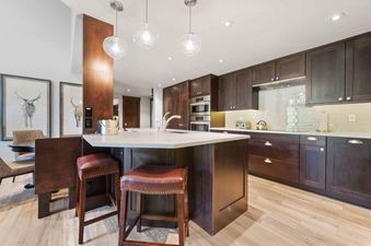 A modern kitchen at The Charter B440 with dark wood cabinets, light countertops, a large island with pendant lighting, and stainless steel appliances.