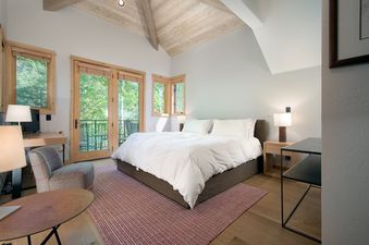 A bright bedroom at Moose Creek 15 featuring a king bed and glass doors that lead to a balcony surrounded by green trees.