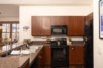 A modern kitchen with wood cabinets, black appliances, granite countertops, and a double sink.