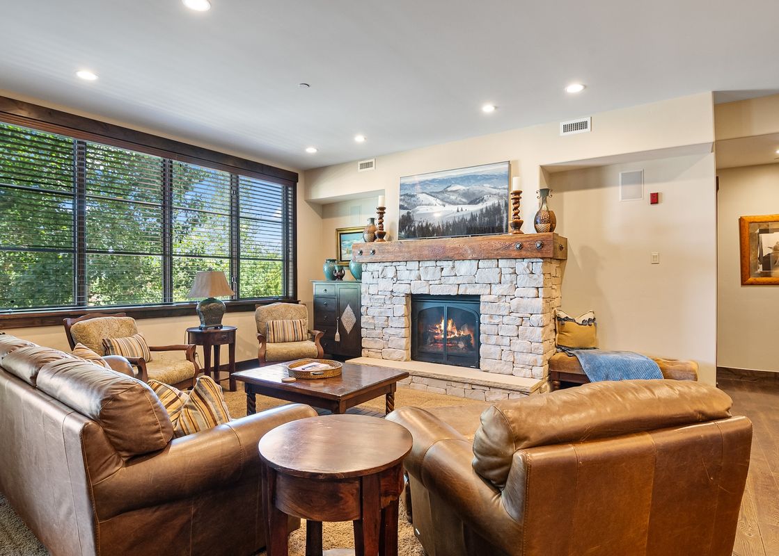 The living area of Silver Star 1104 features comfortable leather sofas, a stone fireplace, and large windows with a view of lush greenery.
