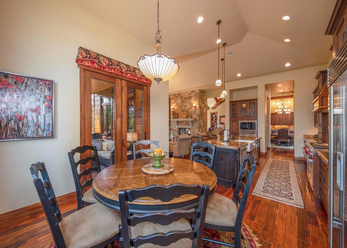 A dining area with a round wooden table and dark chairs, with a view of a living room and kitchen beyond.