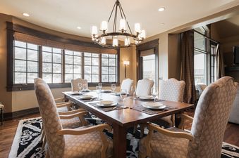 An inviting dining room at Harmony Haus with a large wooden table set for eight, surrounded by upholstered chairs, beneath a grand chandelier.
