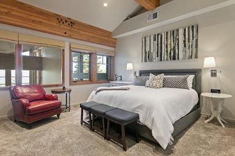 A cozy bedroom at Stag Lodge 10 featuring a king-sized bed, a red leather armchair, and rustic wooden beams.