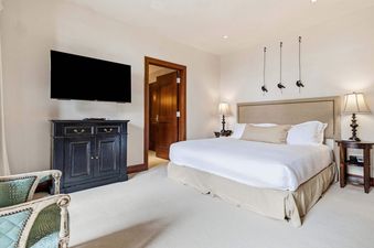 The Solaris 3B West bedroom features a large bed with a white duvet, flanked by two nightstands with lamps, and a wall-mounted TV above a cabinet.