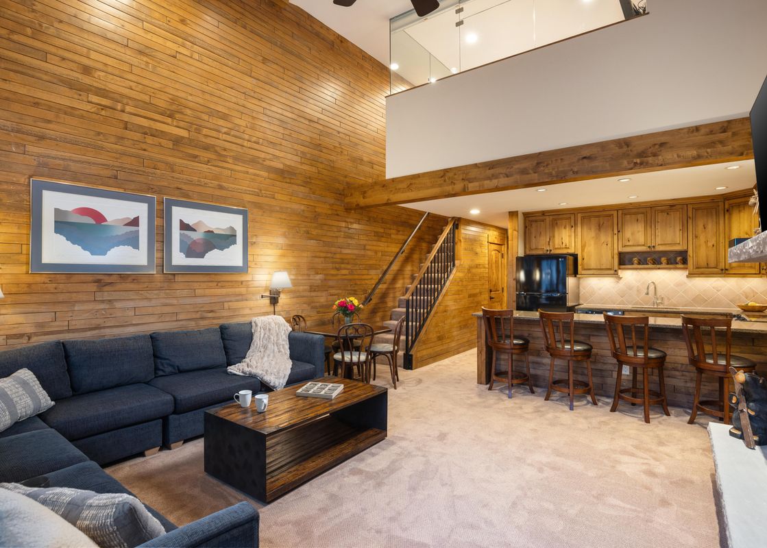 A wide view of the open-concept living room and kitchen at Montaneros 414, featuring a large sectional sofa, coffee table, breakfast bar, and staircase.