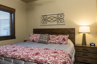 A cozy bedroom in Cana Loft 301 with a wooden bed, patterned bedding, a nightstand with a lamp and clock, and a window with blinds.