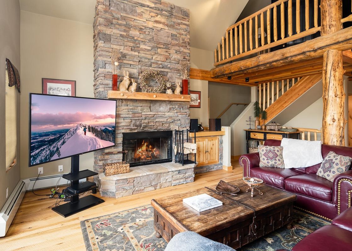 Moonlight Basin 6 Mountain Home Road features a living room with a large flatscreen TV, a stone fireplace, and comfortable leather sofas.