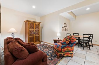 A cozy lounge and dining area featuring a rust-colored sofa, a colorful patterned armchair, a wooden cabinet, and a dining table with four chairs.