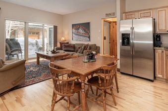 A modern and inviting dining area and living room in Telemark 514, featuring a wooden dining table with chairs, a comfortable sofa, and a large window looking out onto a snow-covered patio.