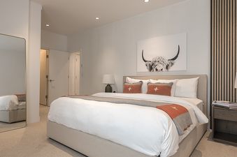 A cozy king-size bedroom at Axiom Retreat featuring a plush white bed with burnt orange accents, a highland cow art piece, and a wooden slat accent wall.