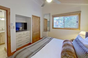A cozy bedroom in Crestwood 2307 with a bed, dresser, flat-screen TV, and an open doorway to a bathroom.