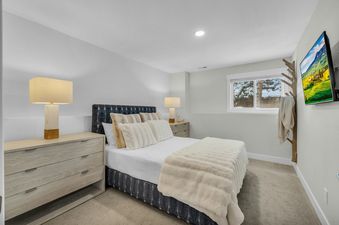 The bedroom in Last Run Luxury features a queen bed with plush white and beige pillows, light wooden nightstands, and soft lighting from two rectangular lamps, creating a serene and comfortable retreat.