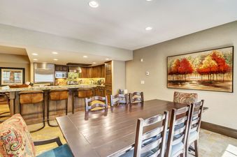 A spacious dining area with a long wooden table and chairs is next to a modern kitchen with a breakfast bar.