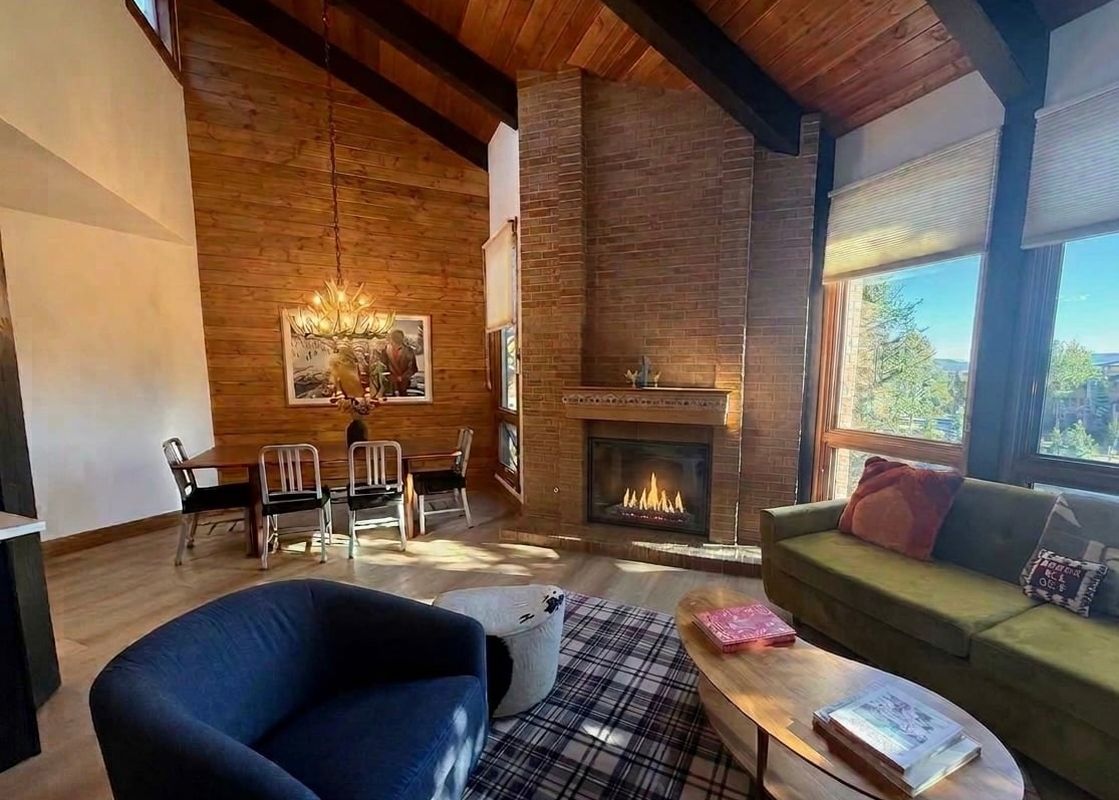 The cozy living area at the Lodge at Steamboat F303 featuring a brick fireplace, high wood ceilings, and comfortable seating.