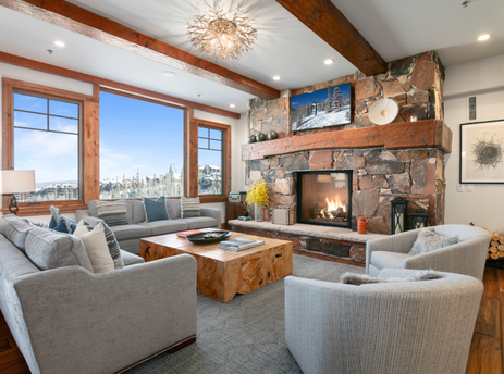 The living room of Grand Lodge Three Bedroom Deluxe 408 features a large stone fireplace and a view of the mountains from the large windows.