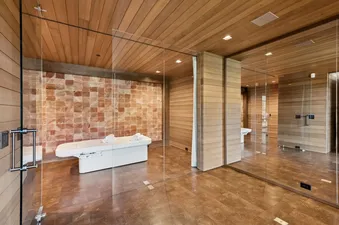 A spa room featuring a white spa bed against a pink Himalayan salt brick wall, enclosed by glass walls with wooden slat details.
