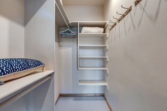 A well-organized closet at the American Flag Solamere features shelves, hanging rods with hangers, golden wall hooks, and a decorative pillow on a lower shelf.