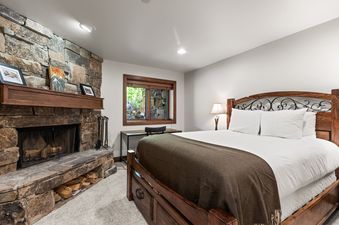 A cozy king bedroom at Slopeside Deer Valley features a wooden bed, stone fireplace, and a desk under a window.