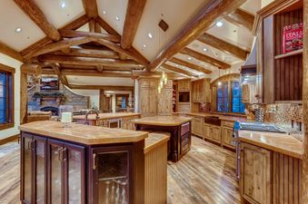 The Ski Hi Lodge kitchen features rich wooden cabinetry, exposed log beams, and a large central island with seating, creating a cozy and rustic atmosphere.