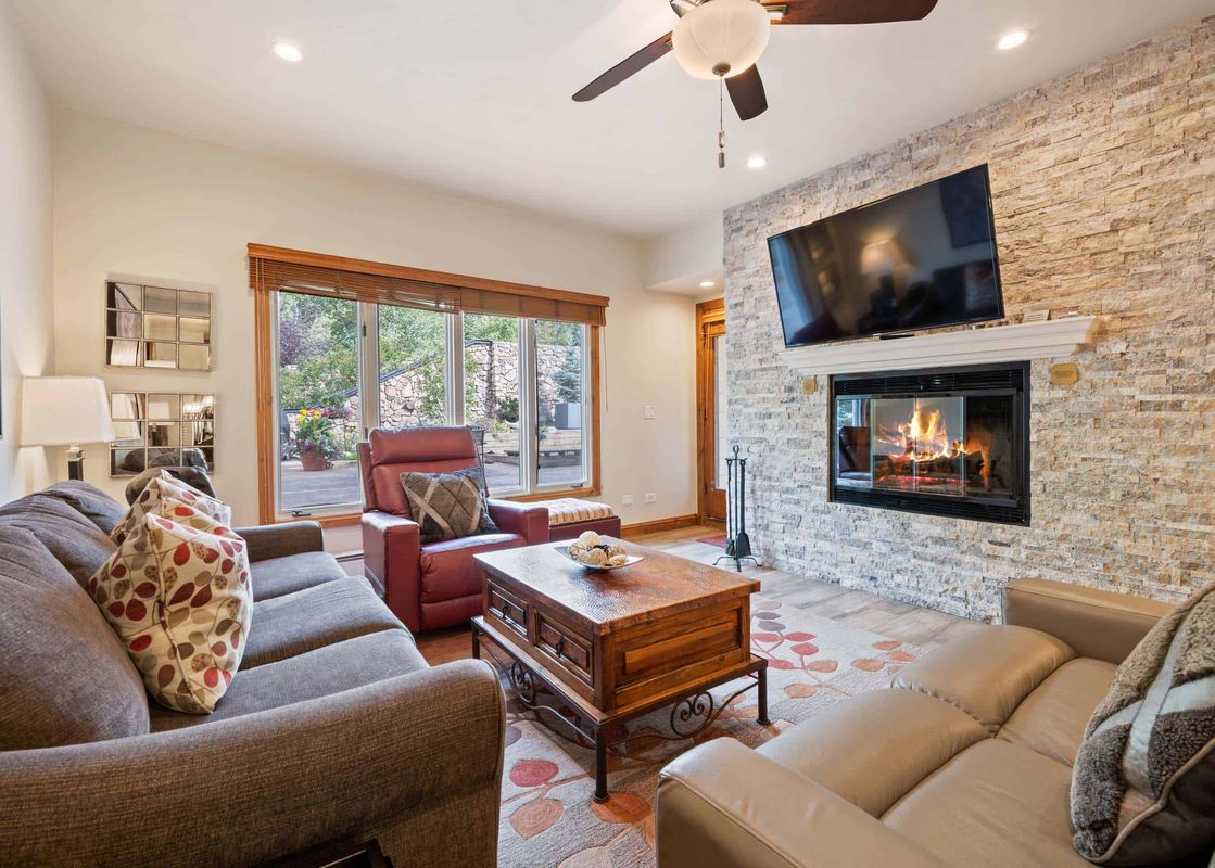 A cozy living room at The Charter F2505 with a stone fireplace, flat-screen TV, comfortable sofas, and large windows looking out to nature.