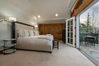 A luxurious king bedroom with white linens and direct access to a private balcony with a bistro table and chairs at Chateau Beaver Creek Residence 202.