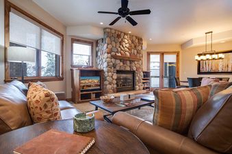 A cozy living room at Chateau Chamonix CX313 features a stone fireplace, leather sofas, a coffee table, and an adjacent dining area.
