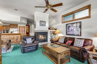 A living room with a fireplace, a large leather couch, a coffee table, and a green carpet.
