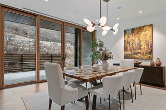 Sophisticated dining room in Founders 1402 featuring a live-edge table, cream chairs, and large sliding doors showing a hillside view.
