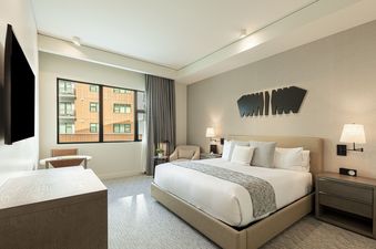A hotel room with a king size bed, a nightstand, and a large window.