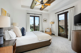 The Lumiere Studio Deluxe bedroom features a plush king bed, a modern TV, floor-to-ceiling windows with a view of the mountains, and an inviting living space.