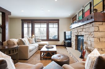 A cozy living room at Silver Star 603 with a large stone fireplace, comfortable sectional sofa, and big windows overlooking a snowy landscape.