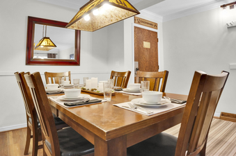Park Station 113 has a wood dining table, six wood chairs, place settings for 6 and the entryway area is behind.