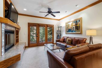 A cozy living room at The Charter E0405 with leather sofas, a fireplace, and a view of trees through French doors.