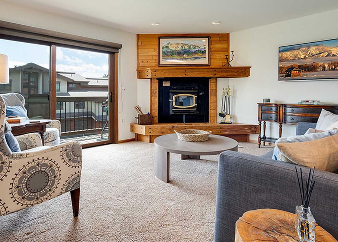 A cozy living room with a fireplace, comfortable seating, a television, and a sliding glass door leading to a balcony.