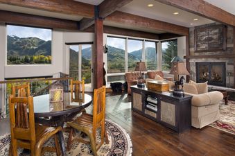 A spacious living area at 185 Nighthawk Dr features wooden beams, a fireplace, and large windows with mountain views, offering both dining and lounging spaces.